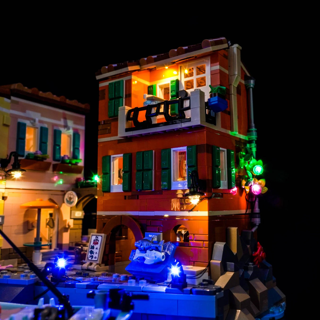 Beleuchtetes Lego-Modell eines Gebäudes mit Balkon und blauen Lichtern am Wasser