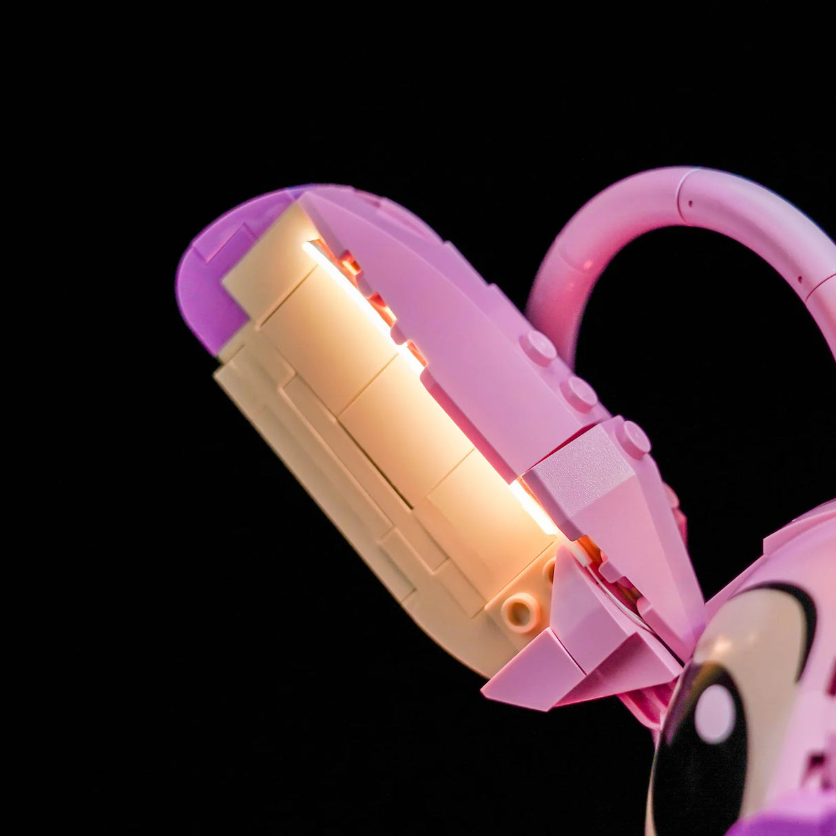Nahaufnahme eines rosa und beigen Lego-Modells mit leuchtenden Elementen auf schwarzem Hintergrund