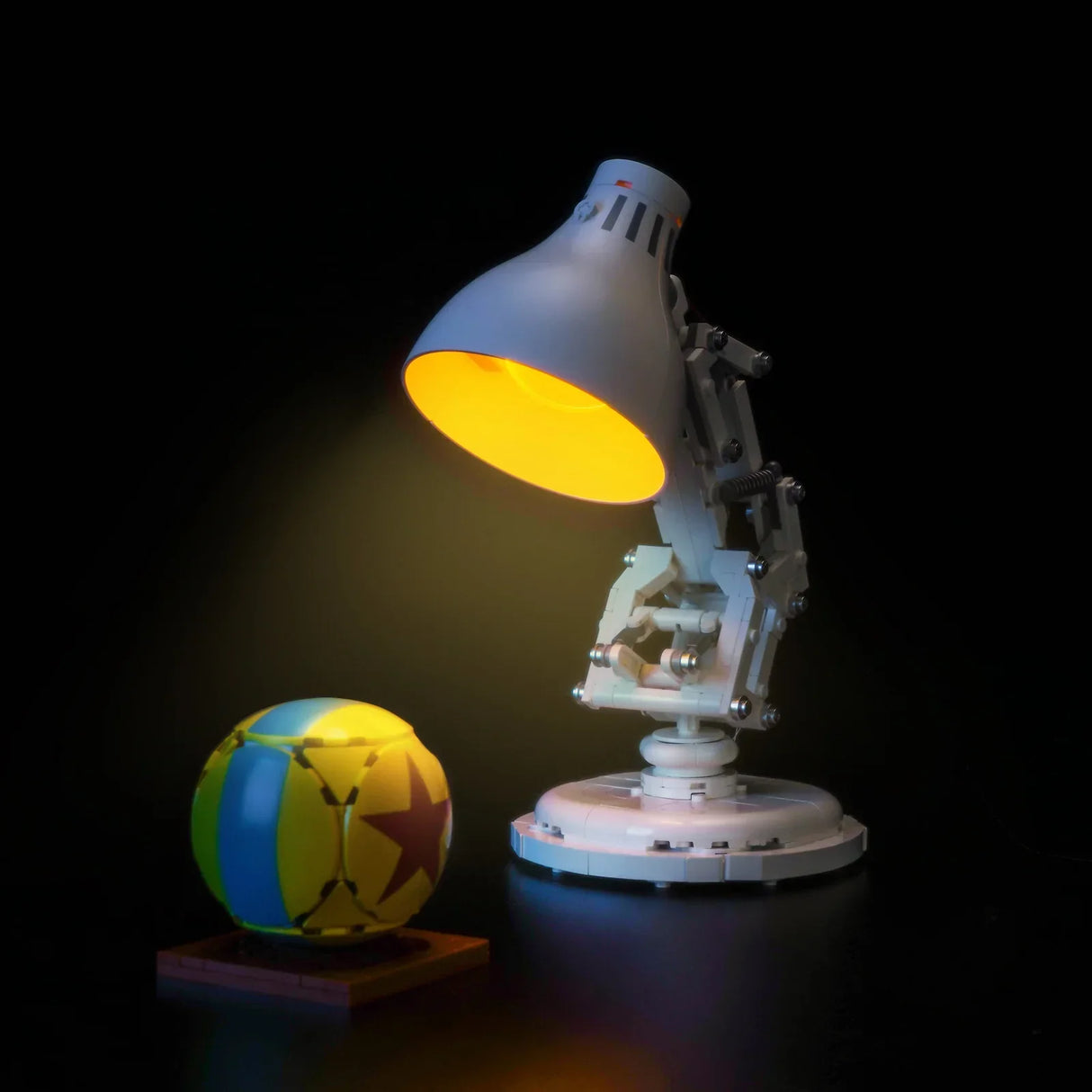 Eine weiße Schreibtischlampe mit gelbem Licht und ein gelb-blauer Ball mit rotem Stern auf schwarzem Hintergrund