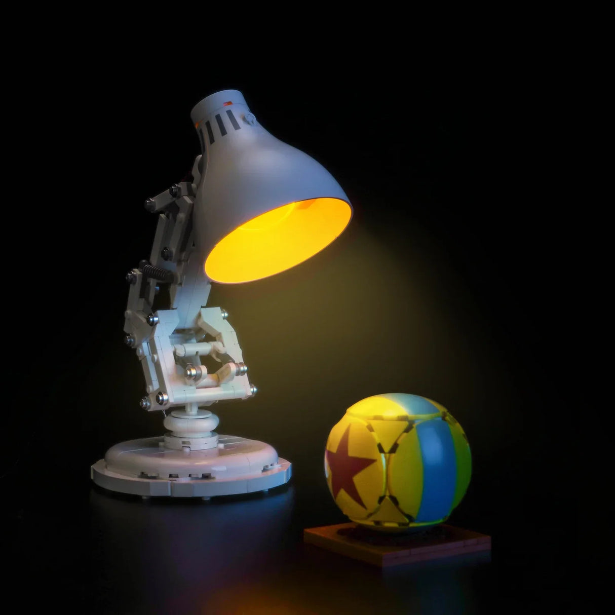 Eine weiße Schreibtischlampe leuchtet einen gelb-blau-roten Ball an