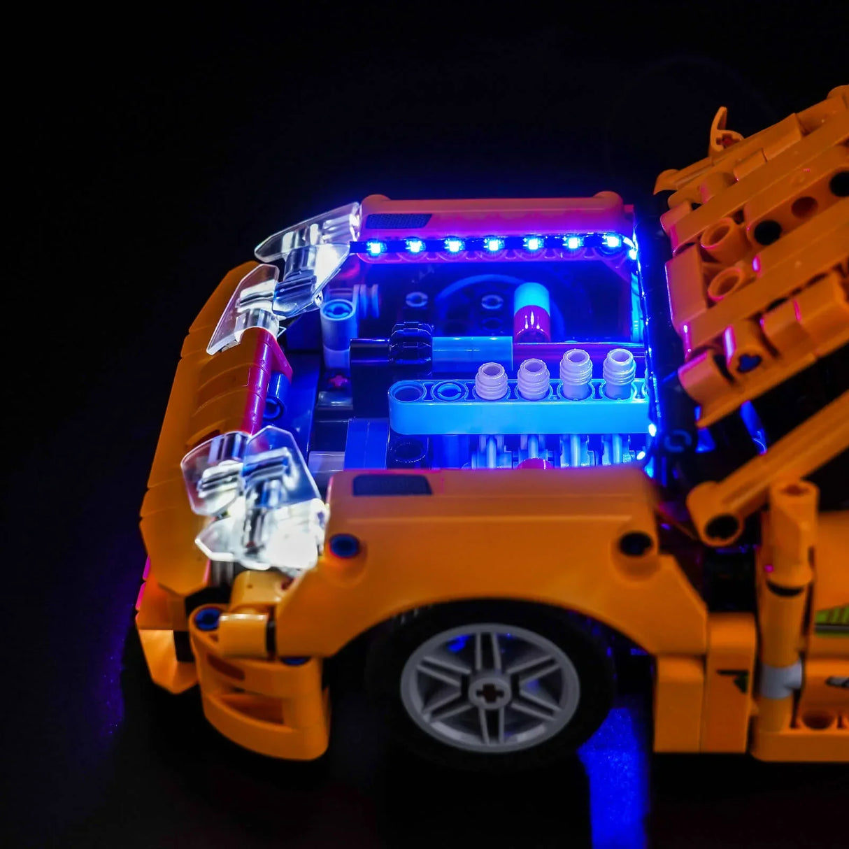 Orangefarbenes Lego-Auto mit leuchtend blauem Motor und Scheinwerfern auf schwarzem Hintergrund