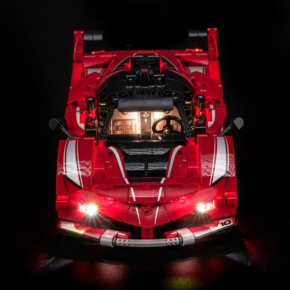 Rotes Spielzeugauto mit weißen Streifen und leuchtenden Scheinwerfern und Innenraum auf schwarzem Hintergrund