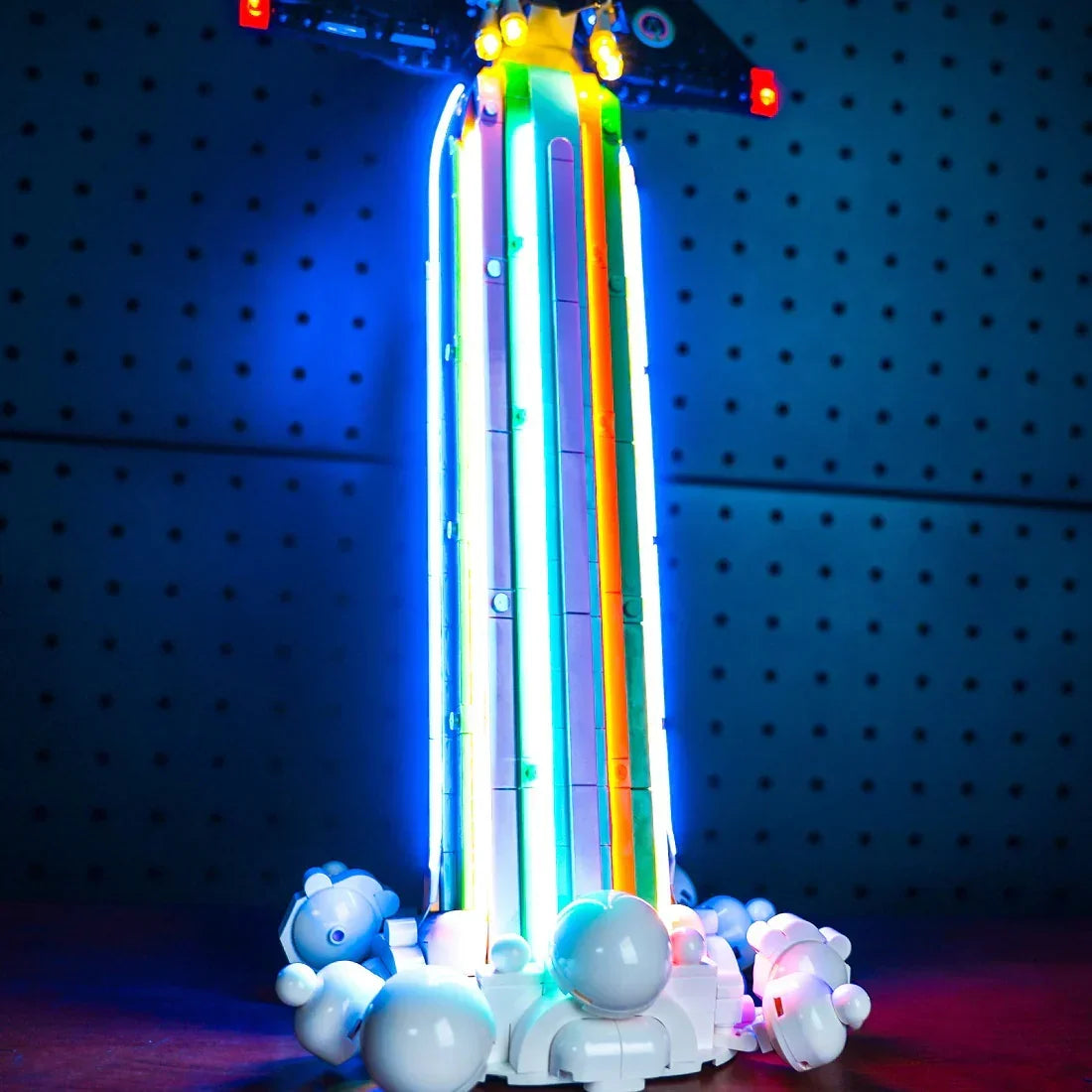 Beleuchtetes Lego Modell eines Raketenstarts mit bunten Lichtstreifen vor einer Lochwand