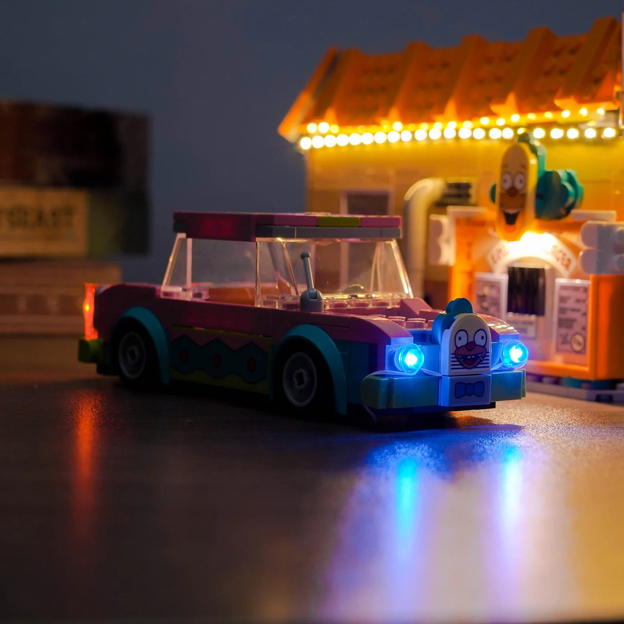 Ein beleuchtetes Lego-Auto mit einem Hasengesicht als Kühlerfigur und einem beleuchteten Lego-Gebäude im Hintergrund
