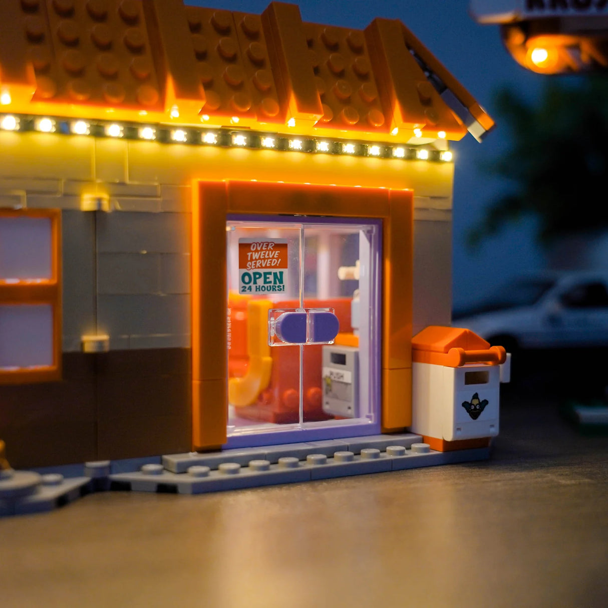 Nahaufnahme eines beleuchteten Lego-Gebäudes mit einem "Open 24 Hours"-Schild an der Tür