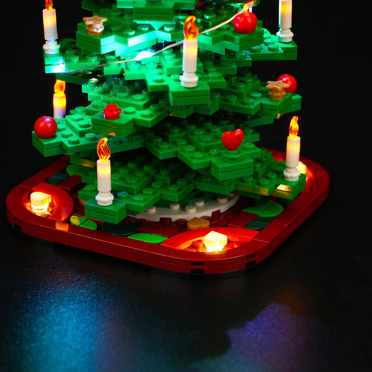 Beleuchteter LEGO Weihnachtsbaum mit roten Kugeln und Kerzen auf rotem Sockel