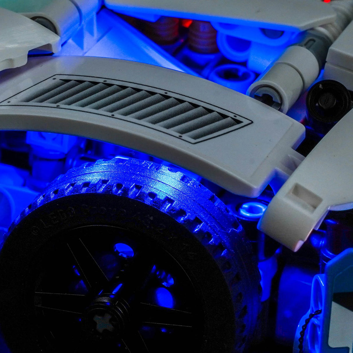 Nahaufnahme eines LEGO-Modells mit blauer Beleuchtung, die ein Rad und Lüftungsschlitze hervorhebt