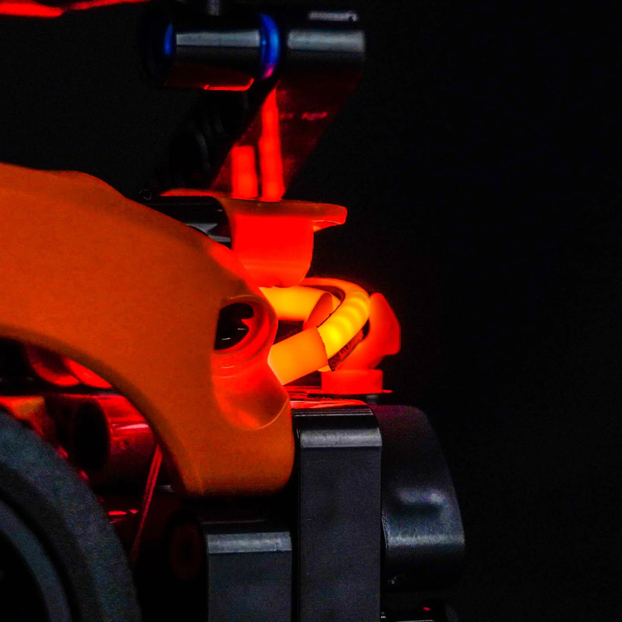 Nahaufnahme eines leuchtenden orangefarbenen Fahrradteils mit roten und gelben Lichtern im Dunkeln