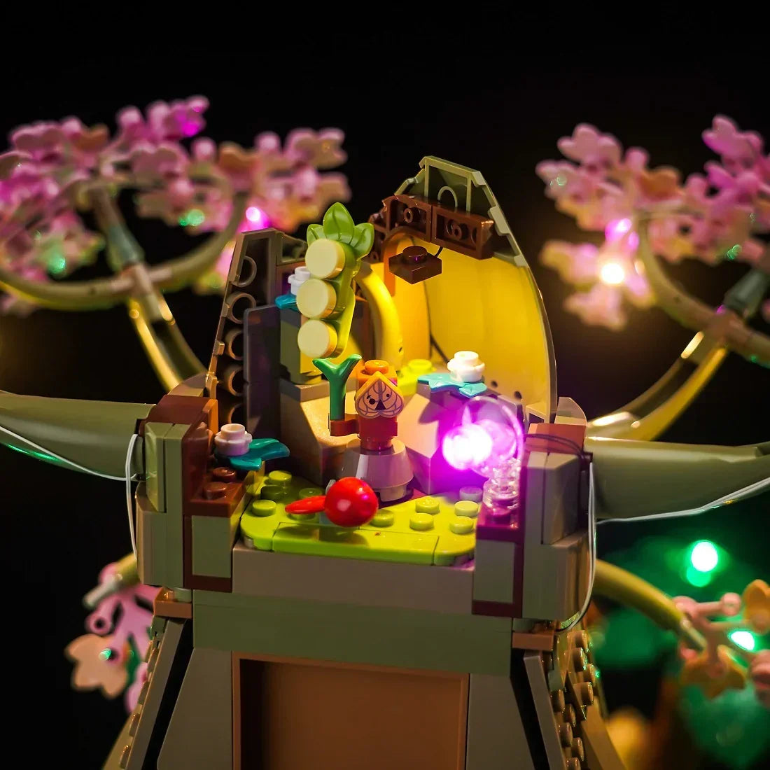 Beleuchtetes Lego Modell eines Baumes mit rosa Blüten und einer kleinen Figur im Inneren