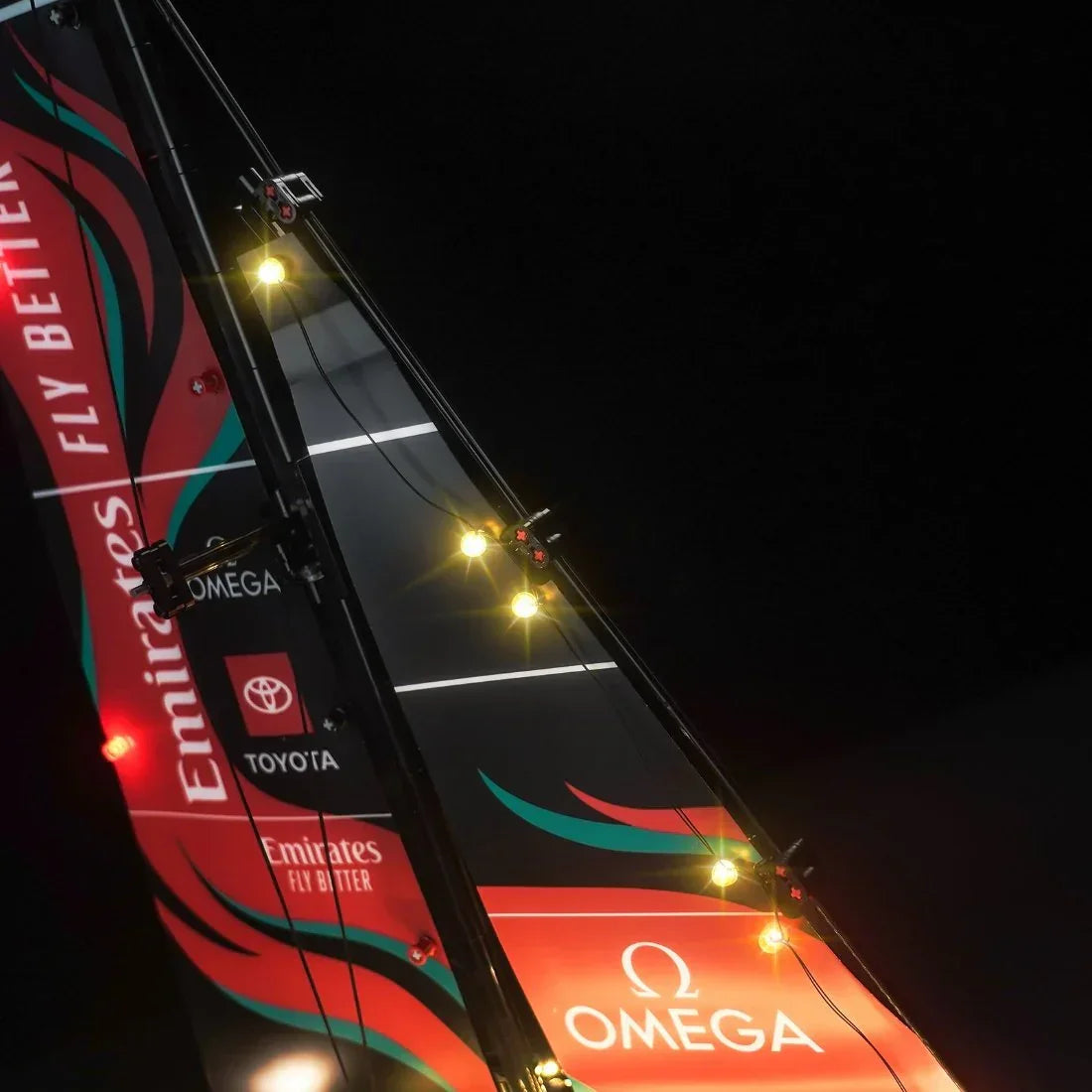 Segel eines Rennboots mit Logos von Emirates Team New Zealand Omega und Toyota bei Nacht