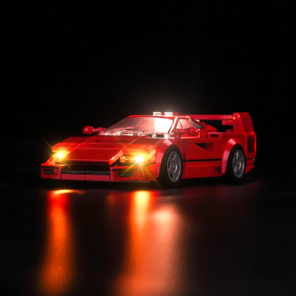 Rotes Lego Modellauto mit eingeschalteter LED Beleuchtung vor schwarzem Hintergrund