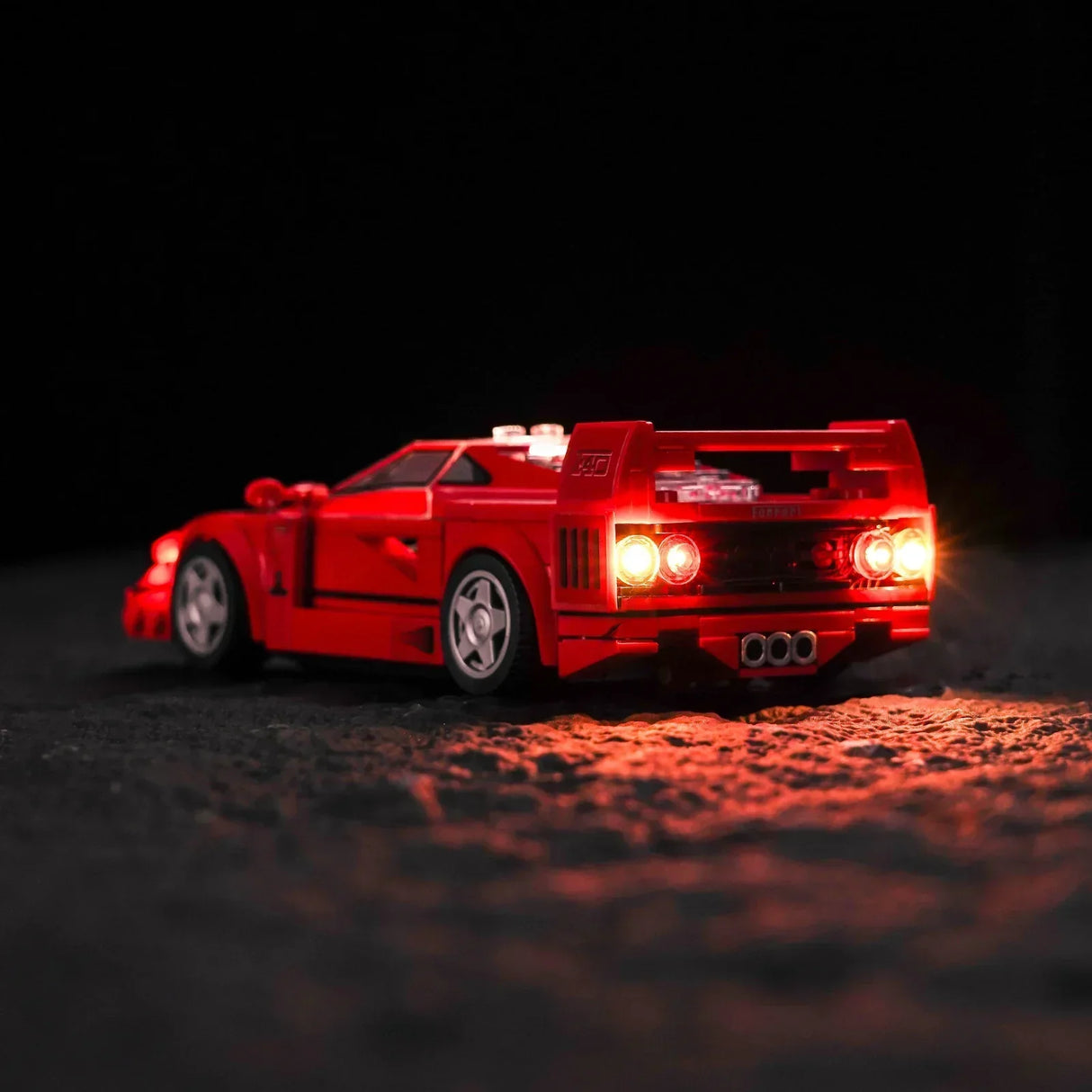 Rotes Ferrari F40 Modellauto aus Klemmbausteinen mit leuchtenden Rücklichtern vor schwarzem Hintergrund