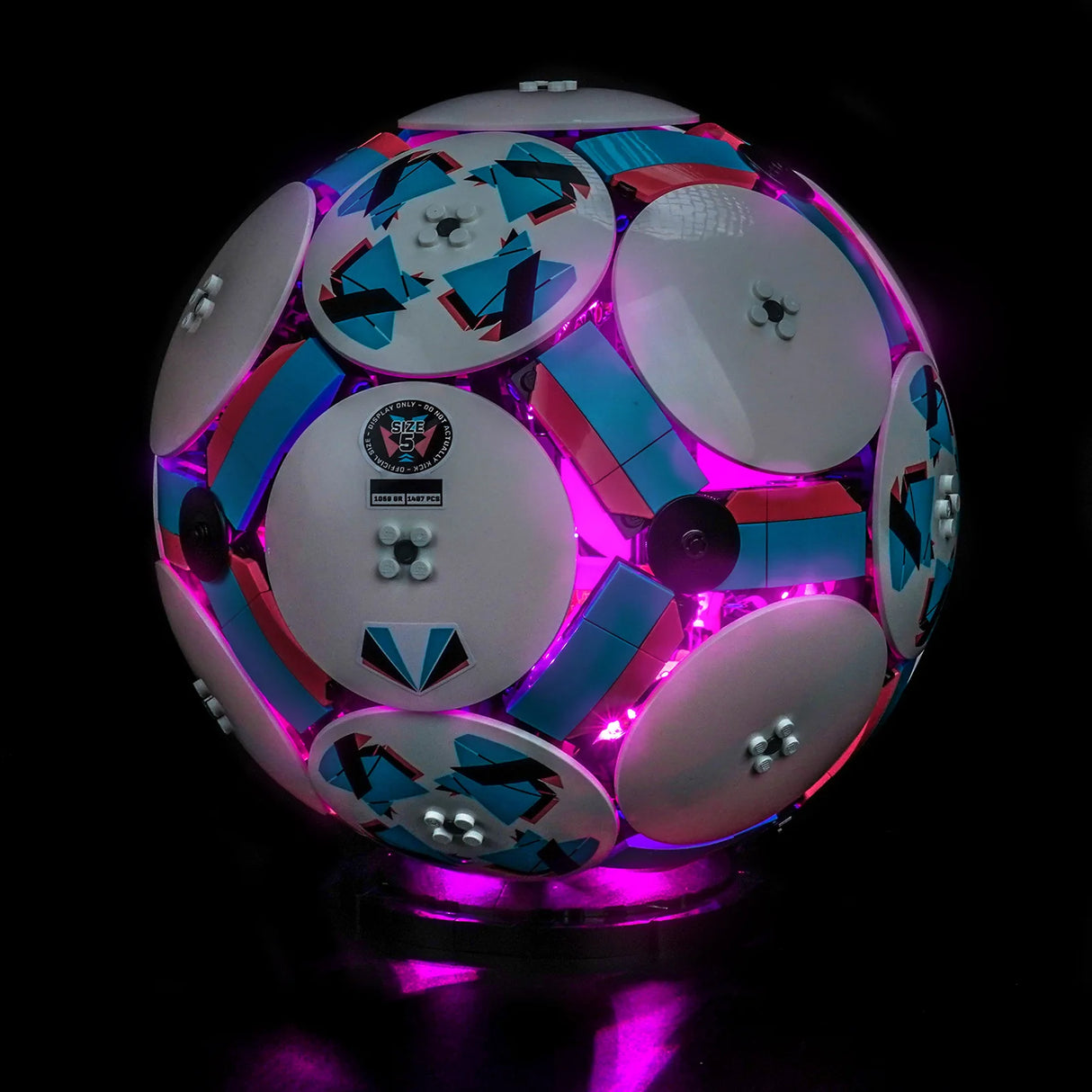 Leuchtender Fußball aus Legosteinen in Pink, Blau und Weiß auf schwarzem Hintergrund
