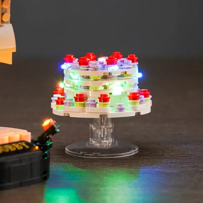Ein beleuchteter Lego-Kuchen mit roten, lila und grünen Details auf einem durchsichtigen Ständer