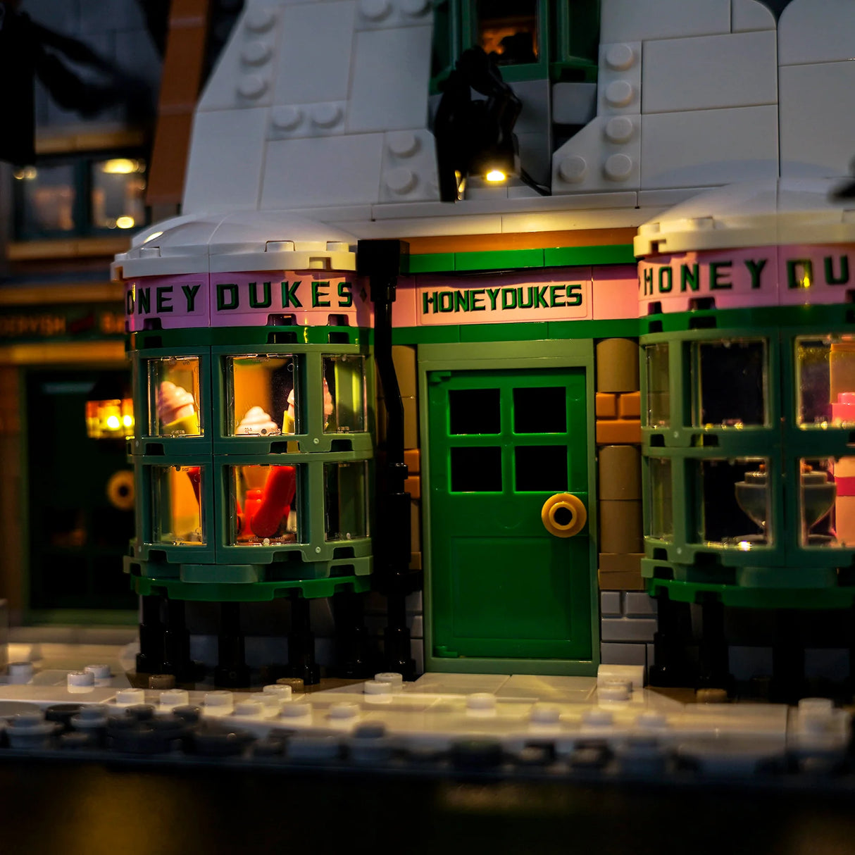 Nahaufnahme des beleuchteten Honeydukes-Gebäudes aus Lego mit grüner Tür und Schaufenstern