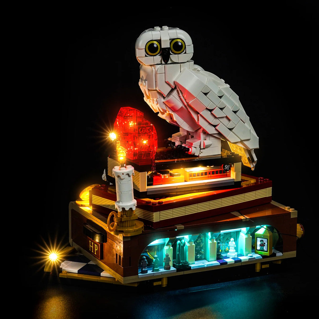 Ein beleuchtetes Lego-Modell von Hedwig auf Büchern mit Hogwarts-Szenen