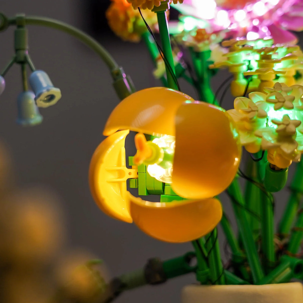 Nahaufnahme einer gelben LEGO Blume mit leuchtendem Inneren und blauen Glockenblumen im Hintergrund