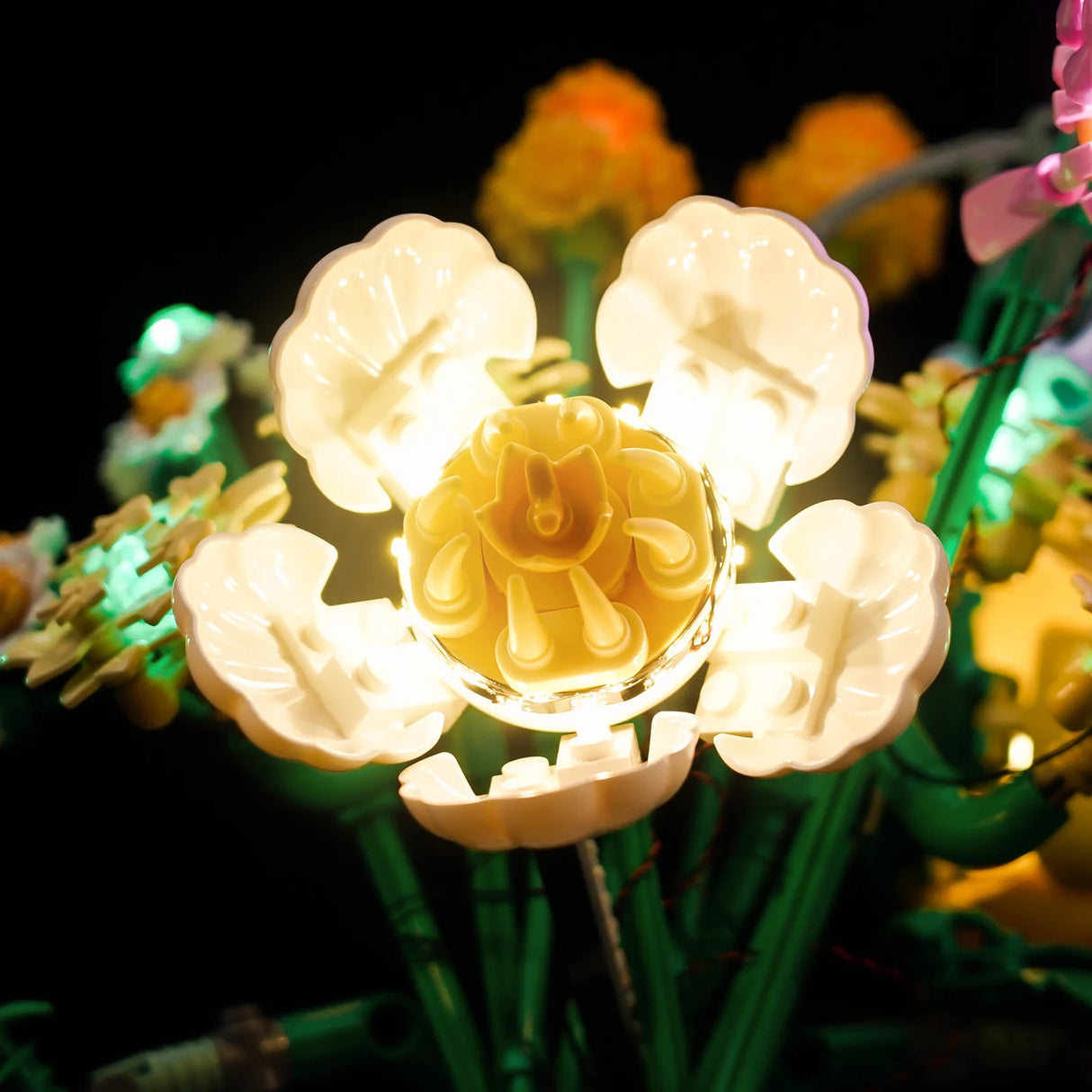 Nahaufnahme einer leuchtenden gelben und weißen LEGO Blume mit grünen Stielen im Dunkeln