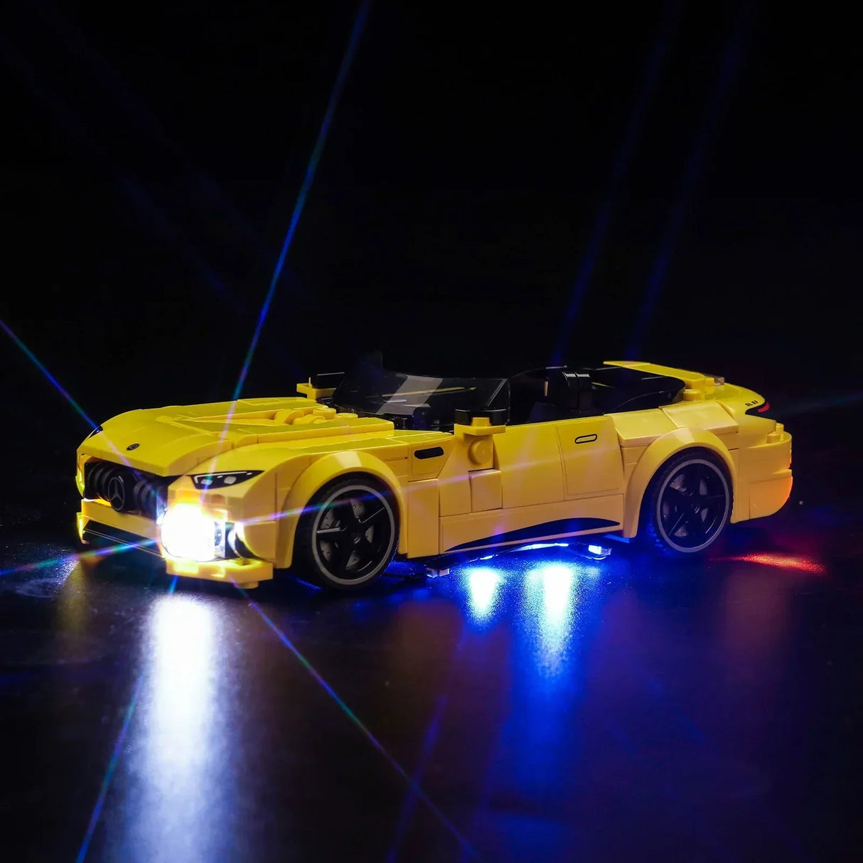 Gelbes Mercedes AMG Modellauto aus Klemmbausteinen mit eingeschalteter LED Beleuchtung vor schwarzem Hintergrund