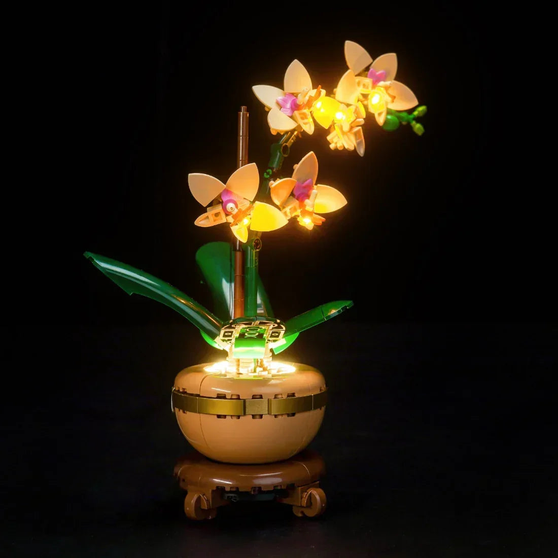 Beleuchtete LEGO Orchidee mit gelben Blüten und grünen Blättern in einem beigen Topf auf schwarzem Hintergrund