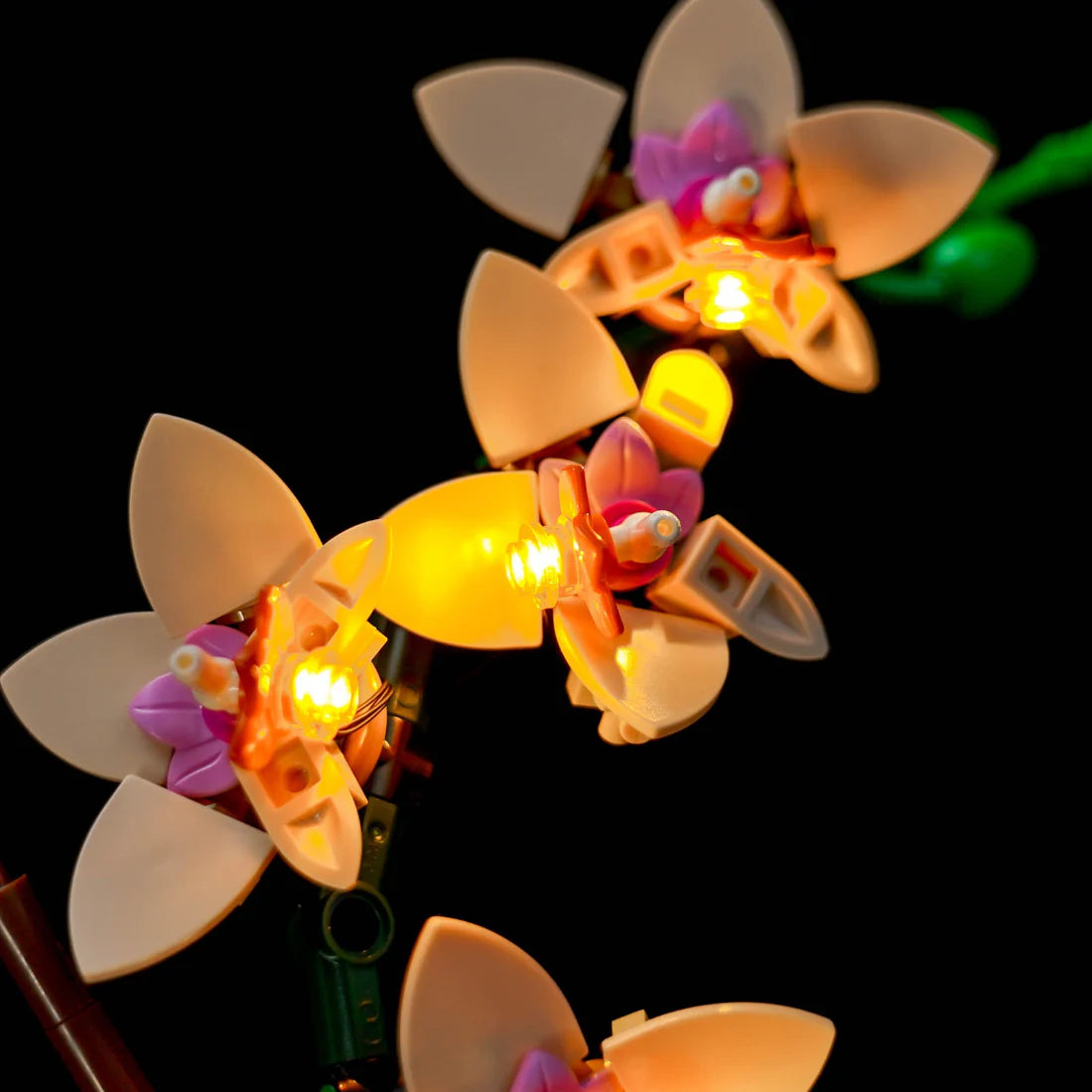 Nahaufnahme von drei leuchtenden Lego-Orchideenblüten mit gelben Lichtern auf schwarzem Hintergrund