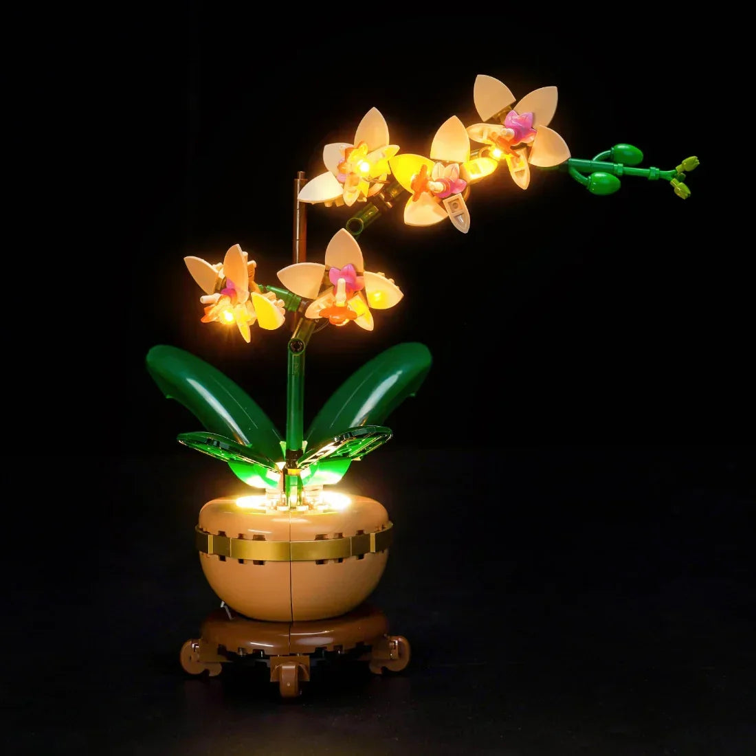 Beleuchtete LEGO Orchidee mit gelben Blüten und grünen Blättern in einem braunen Topf auf schwarzem Hintergrund