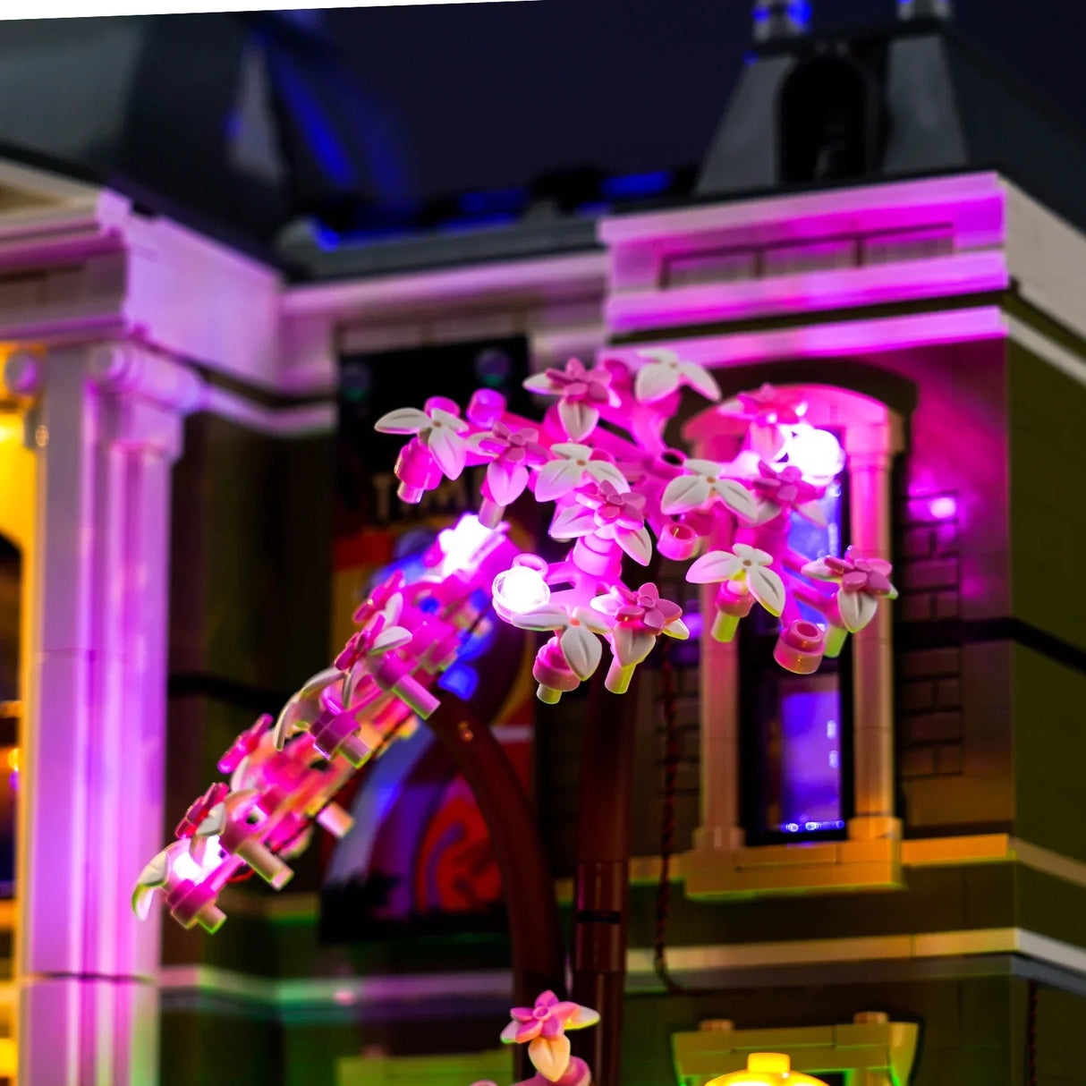 Nahaufnahme eines beleuchteten LEGO Kirschblütenbaums mit rosa und weißen Blüten vor einem Gebäude