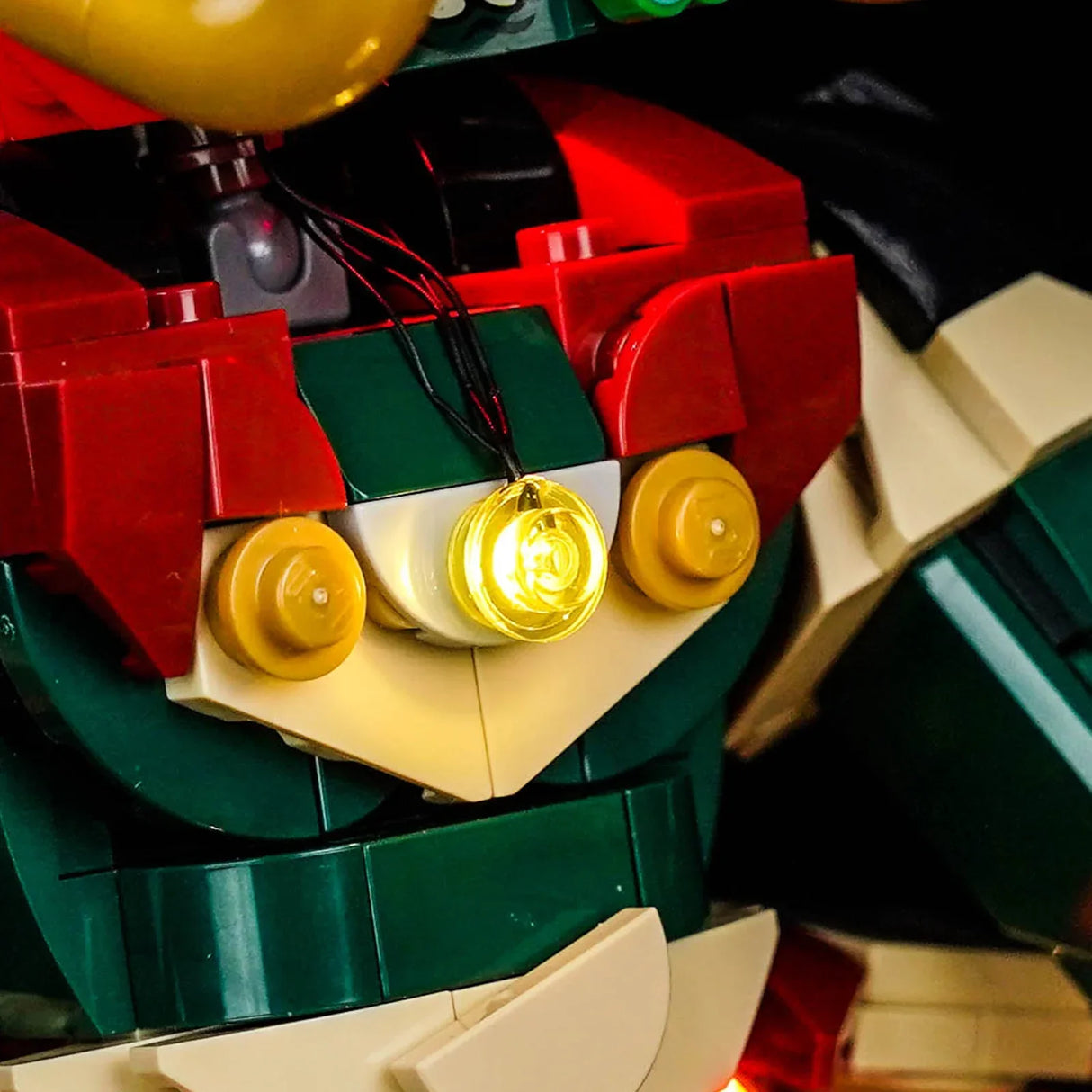 Nahaufnahme eines Lego-Modells mit roten, grünen und beigen Steinen, die von einem gelben Licht beleuchtet werden