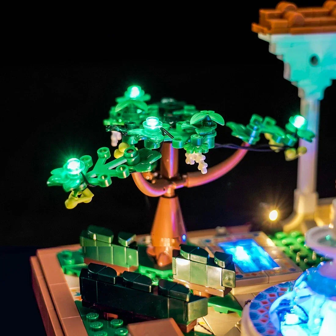 Beleuchteter Lego-Baum mit grünen Blättern und weißen Blüten, daneben ein leuchtender Brunnen