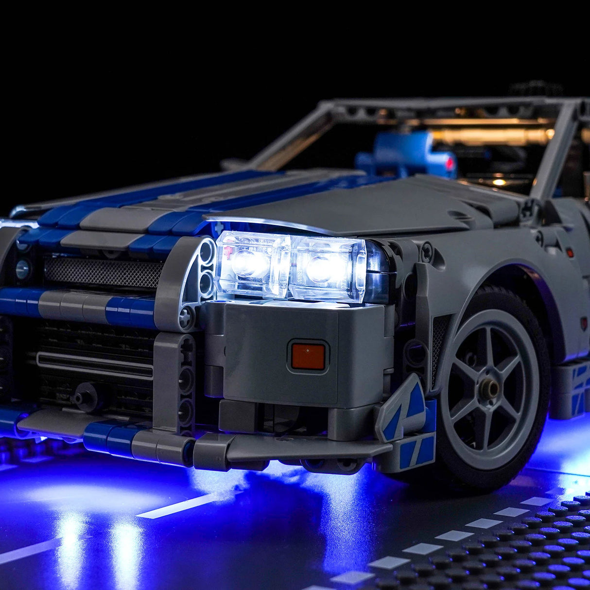 Graues und blaues Lego-Auto mit leuchtenden Scheinwerfern und Unterbodenbeleuchtung auf einer dunklen Oberfläche