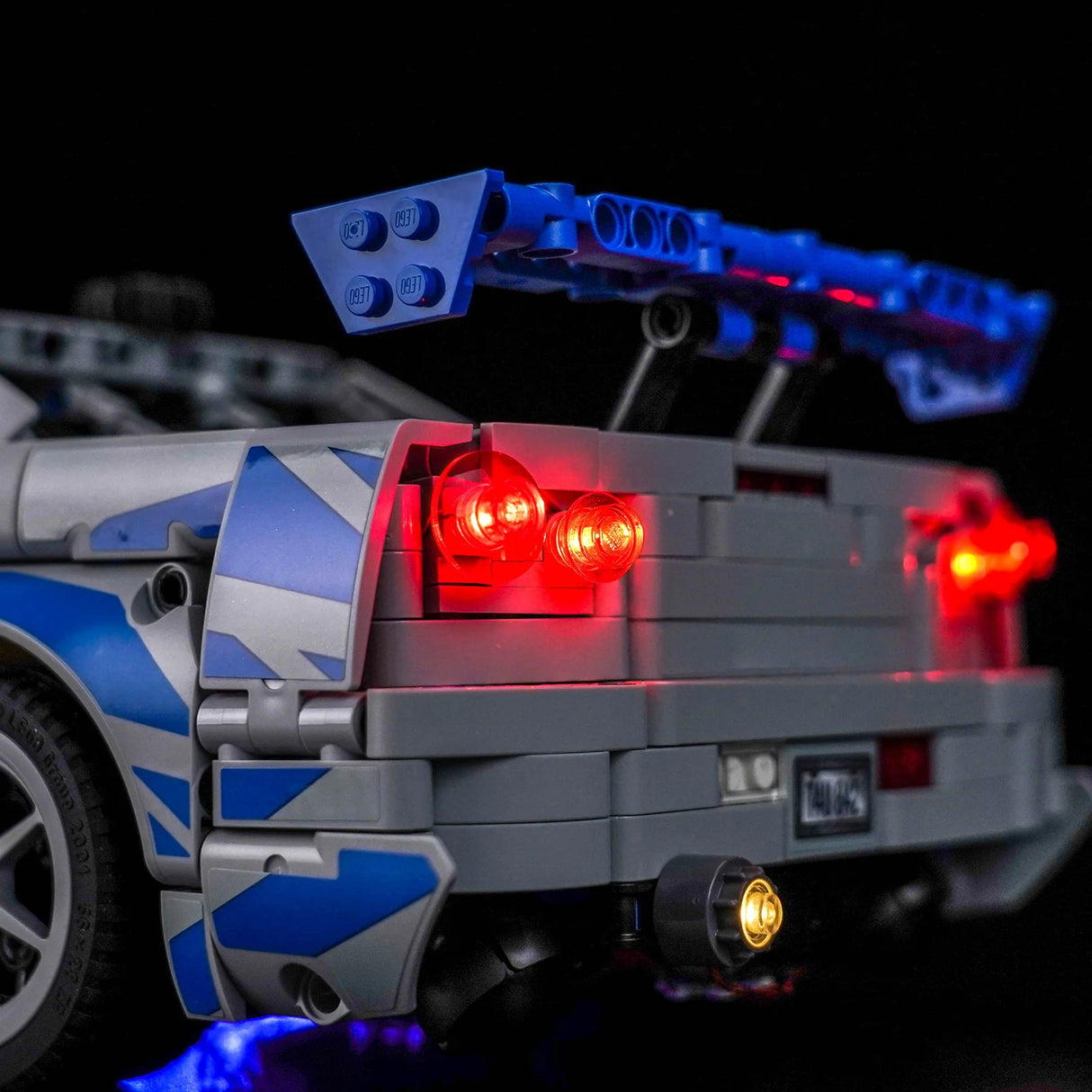 Rückansicht eines grauen Lego-Autos mit blauen Streifen und leuchtenden roten Rücklichtern