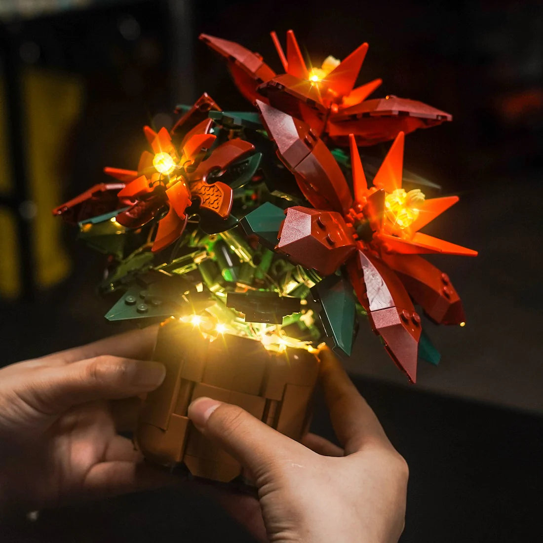 Hände halten einen leuchtenden LEGO Weihnachtsstern in einem Topf