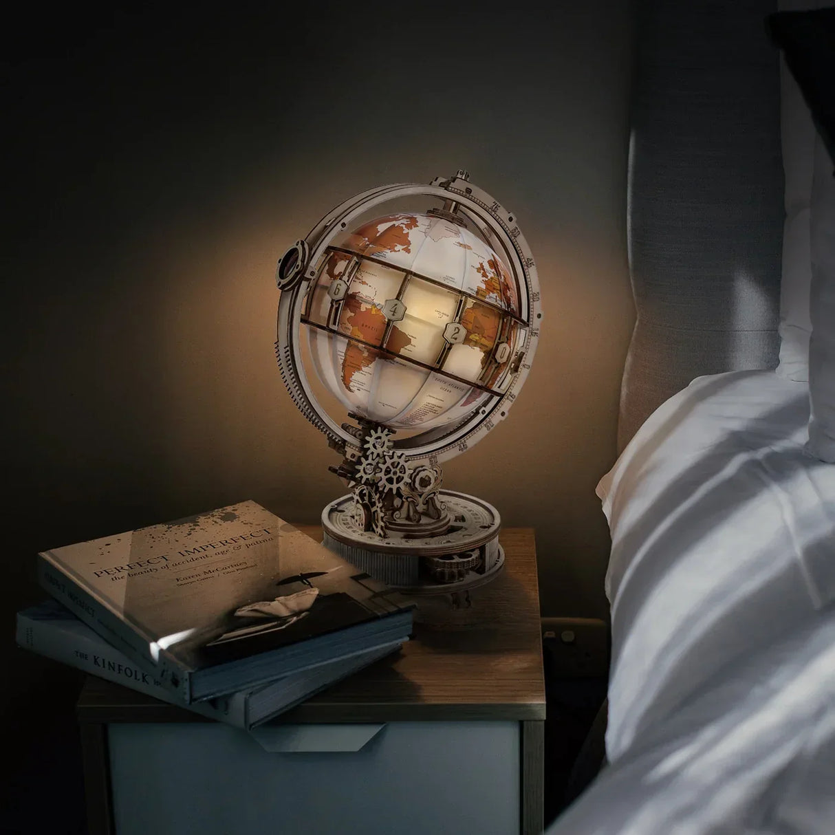 Beleuchteter Globus auf Nachttisch neben Bett mit Büchern