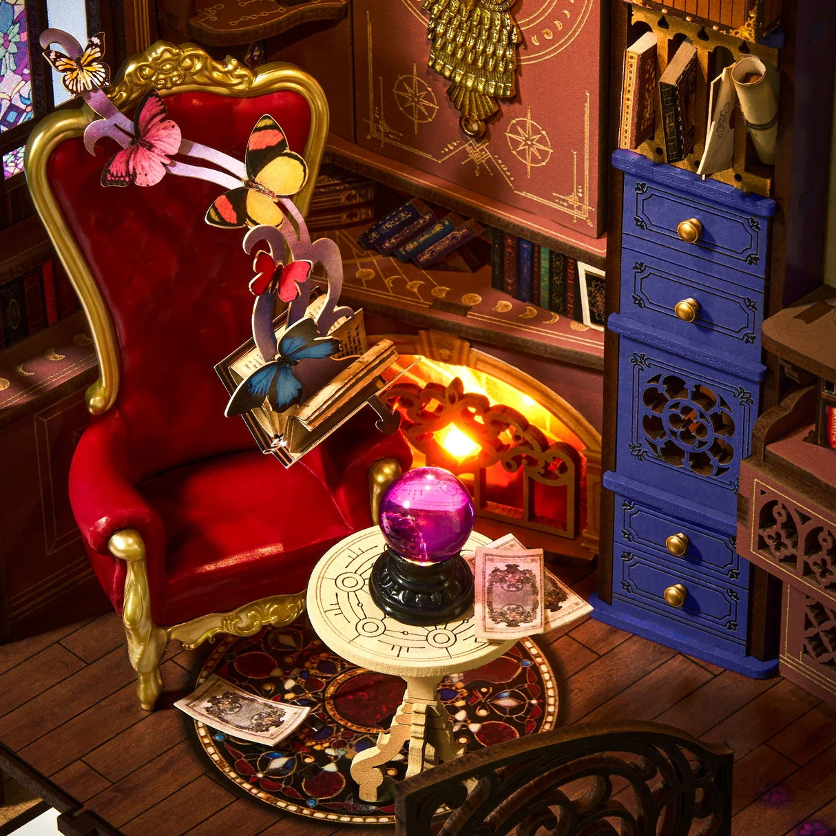 Miniatur-Puppenhauszimmer mit rotem Sessel, blauer Kommode, Kristallkugel auf Tisch und Schmetterlingen