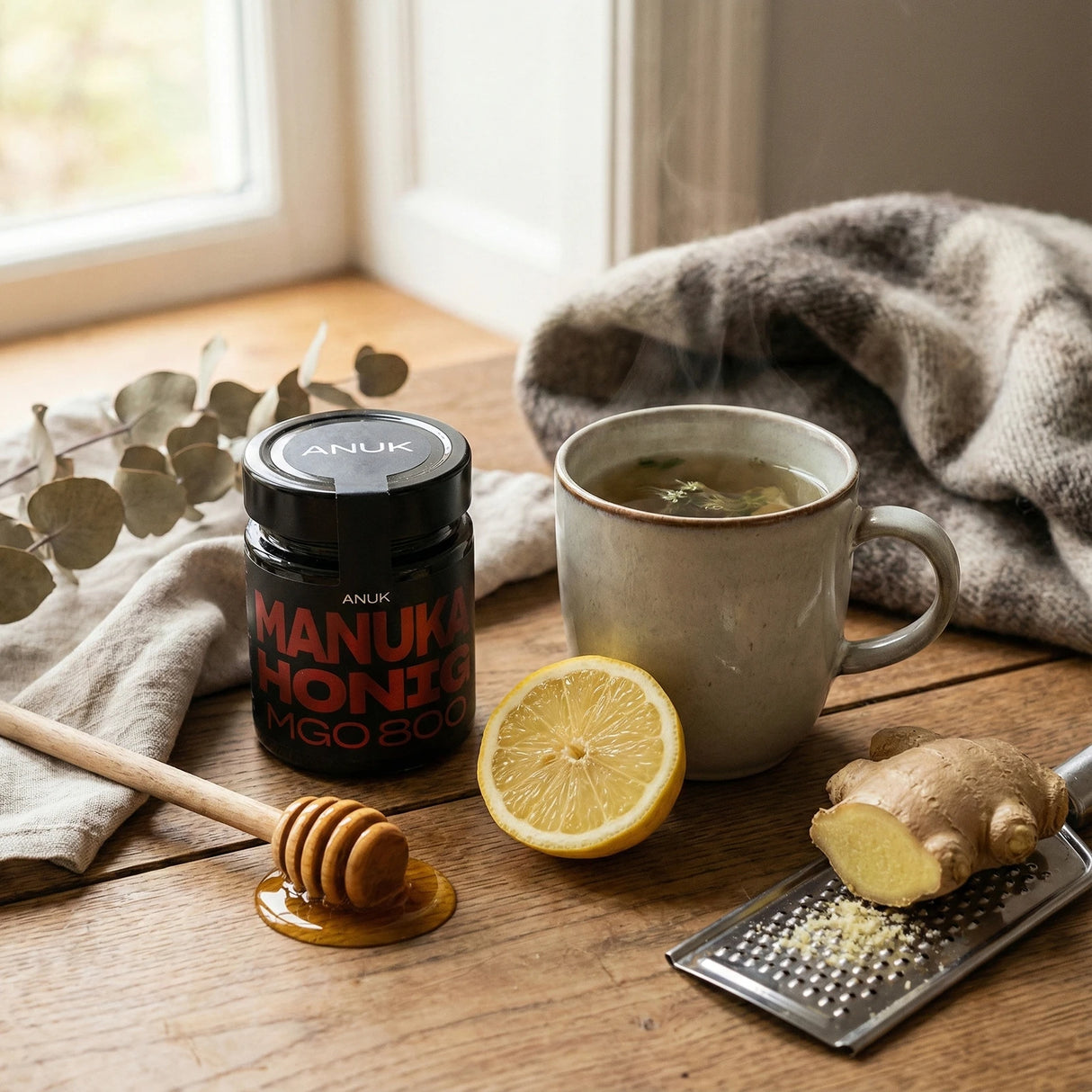 Anuk Manuka Honig MGO 800 Glas, Honiglöffel, Zitrone, Ingwer und Tasse Tee auf Holztisch