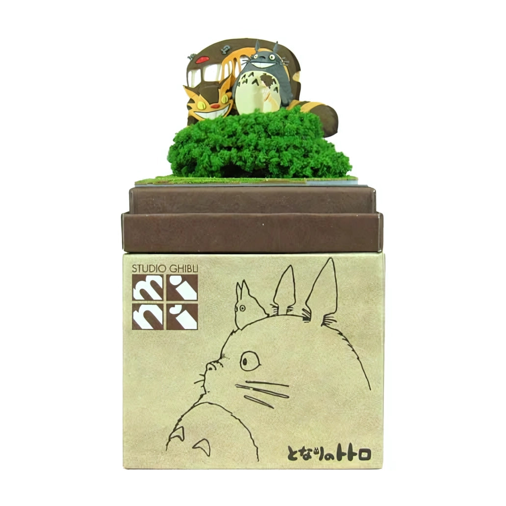 Totoro und Catbus Figuren auf grünem Buschwerk, auf einer braunen Box mit Totoro-Zeichnung