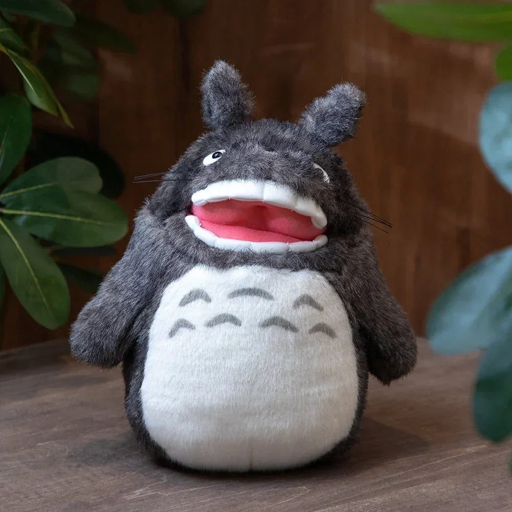 Graues Totoro Plüschtier mit offenem Mund und rosa Zunge auf Holztisch