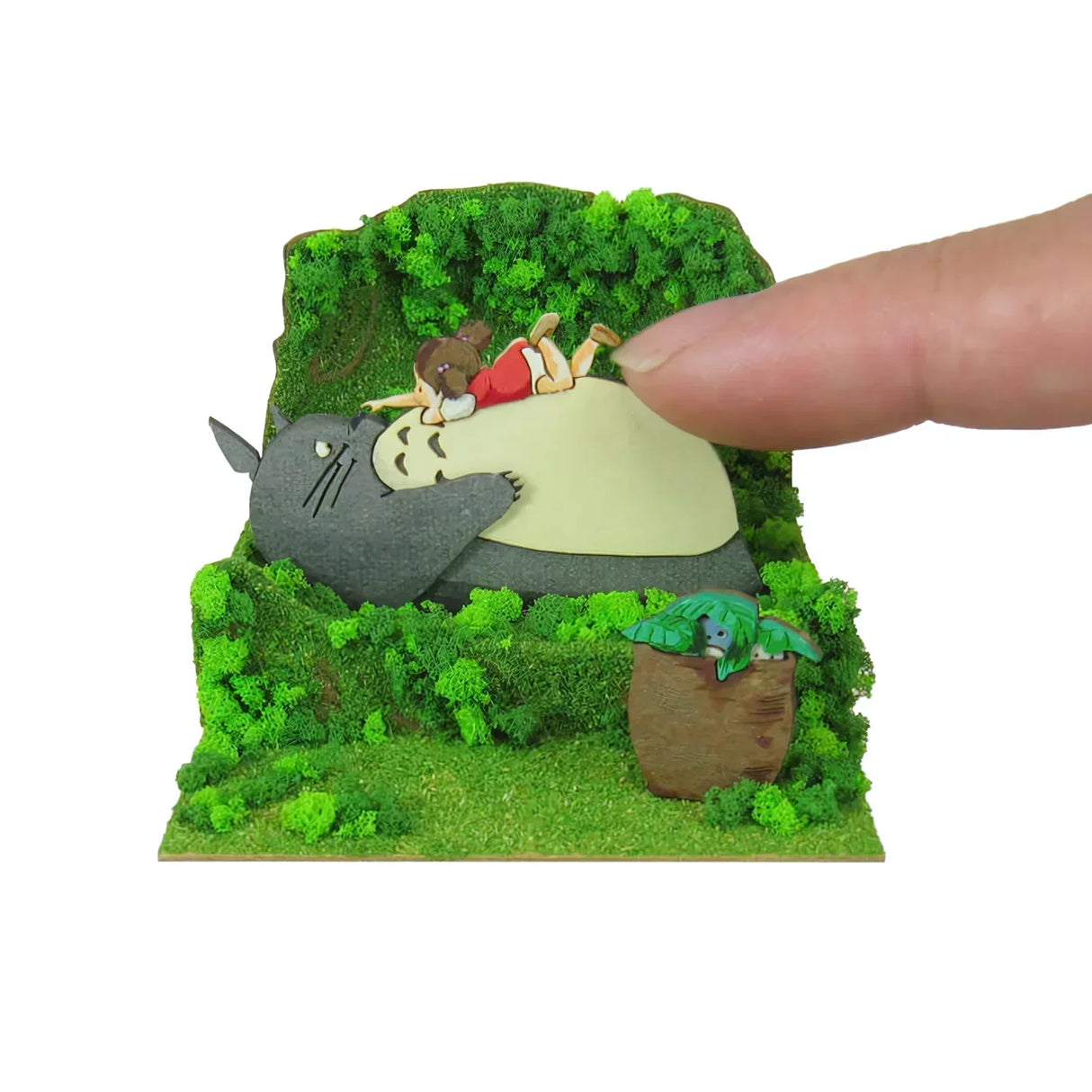 Finger berührt Totoro und Mädchen auf einem Moosbett