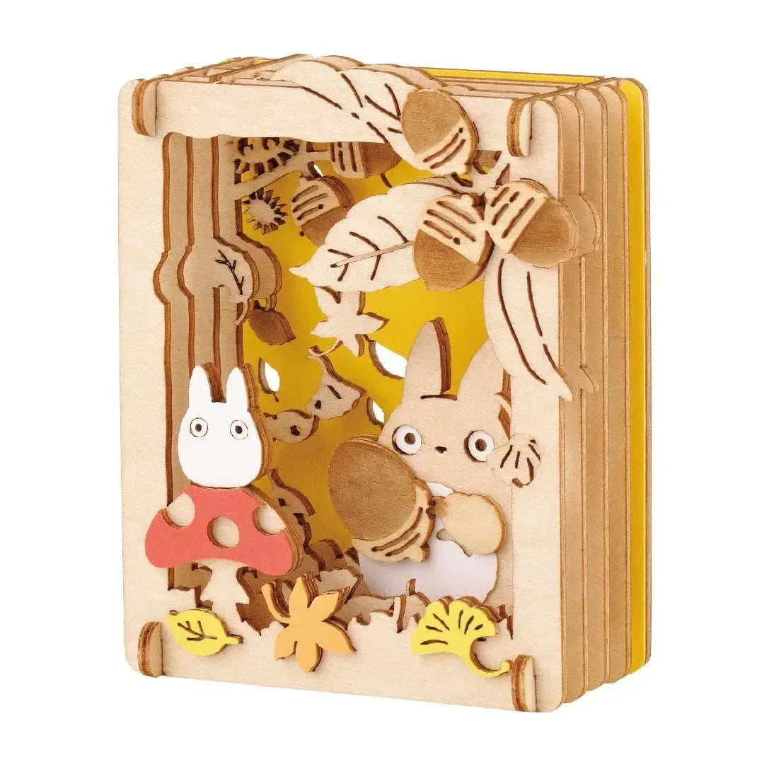 Holz-Diorama mit Totoro-Figuren, Pilzen und Eicheln vor gelbem Hintergrund