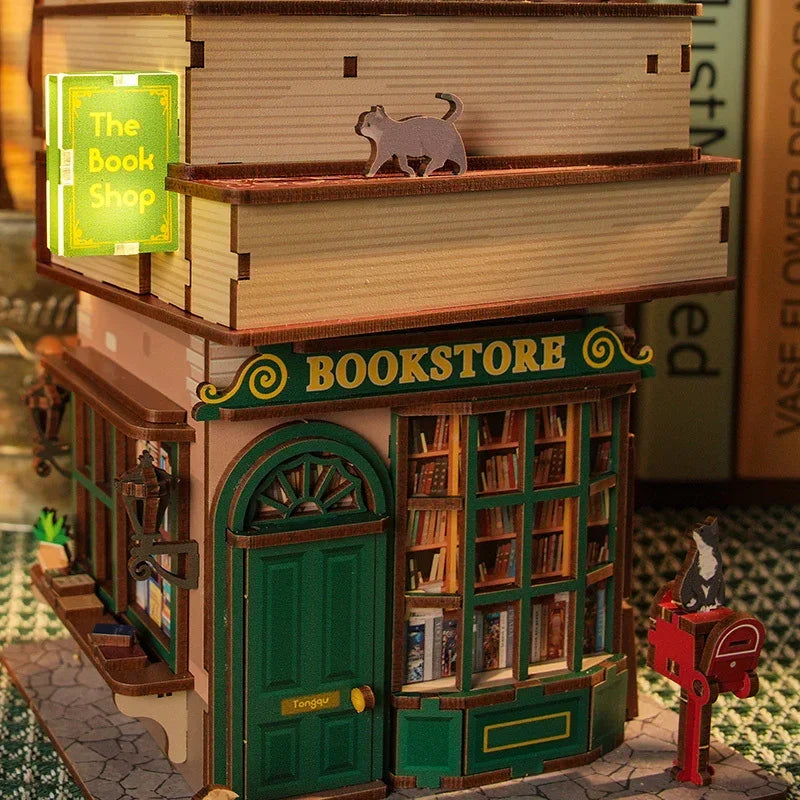 Miniatur-Buchladen-Modell mit grüner Tür und Schaufenstern, darüber gestapelte Bücher und eine Katze