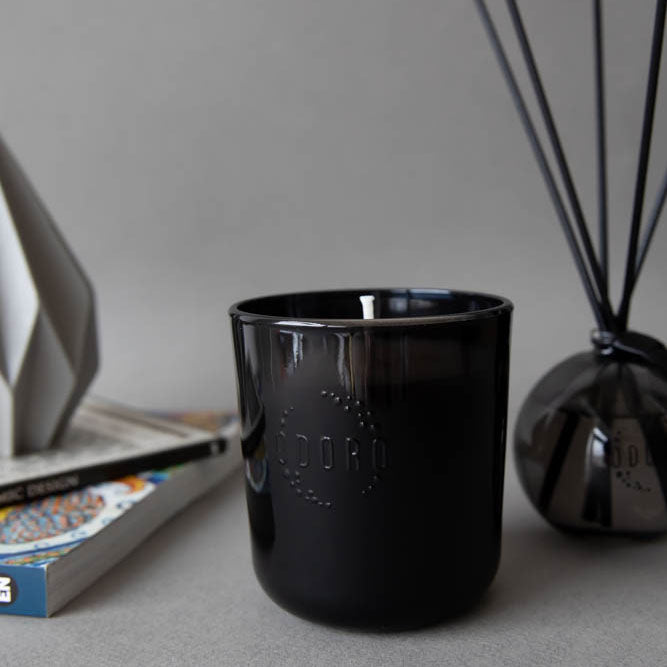 Schwarze Duftkerze im Glas neben einem Raumduft mit Stäbchen