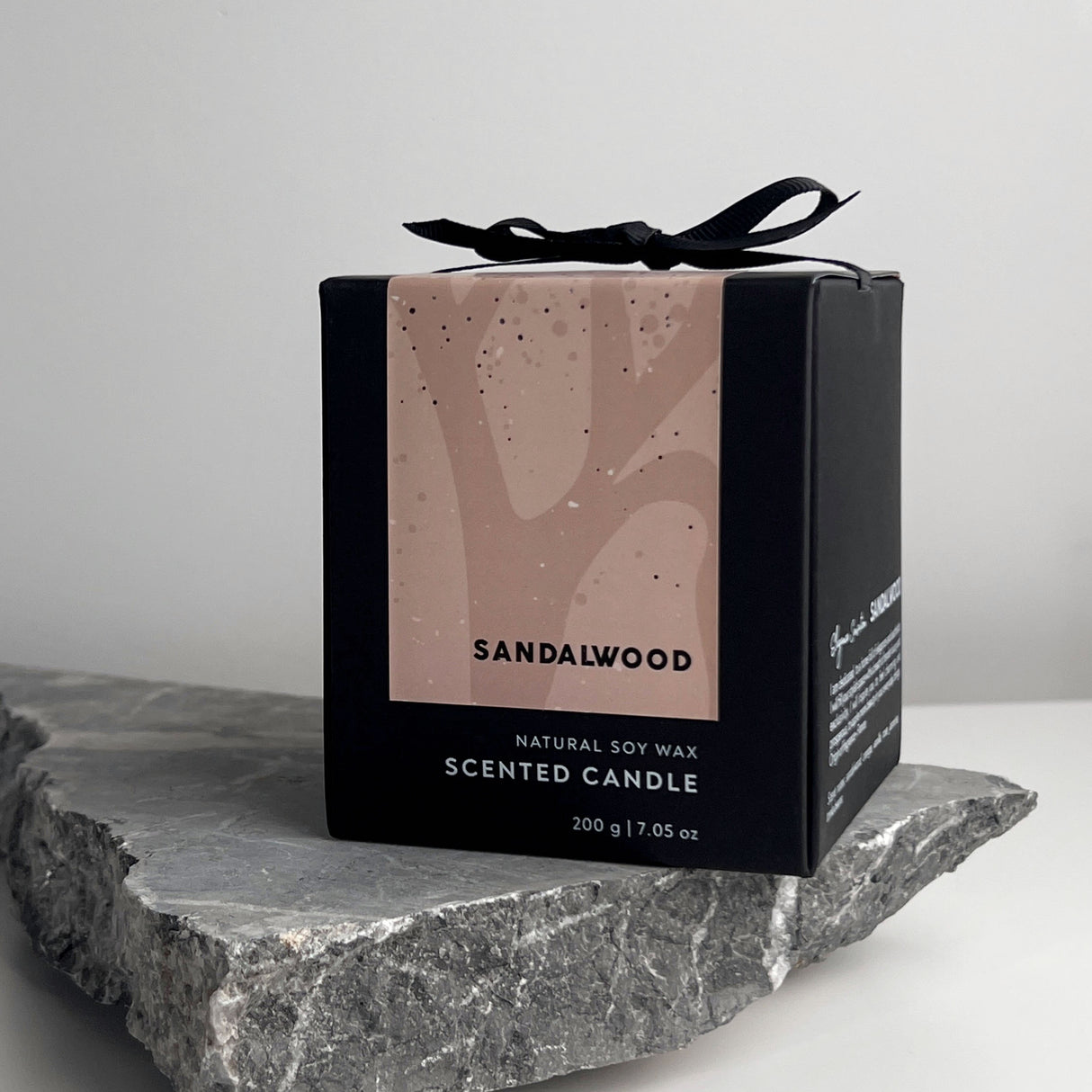 Schwarze Duftkerzenverpackung mit Sandelholz Aufschrift auf einem grauen Stein