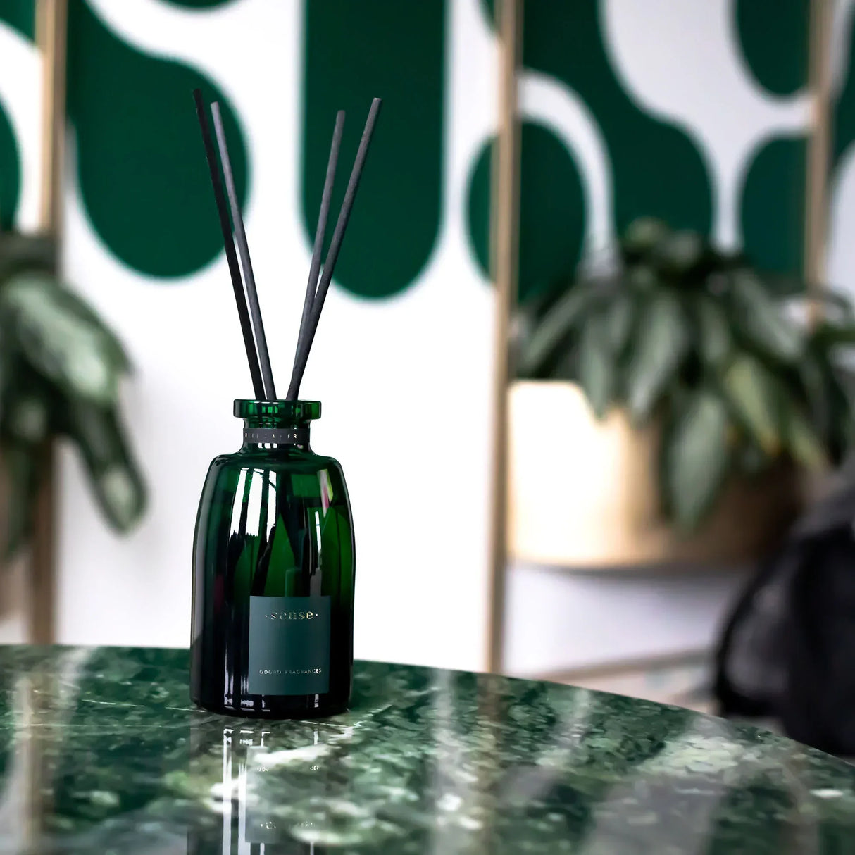 Grüne Glasflasche mit Duftstäbchen auf einem marmorierten Tisch