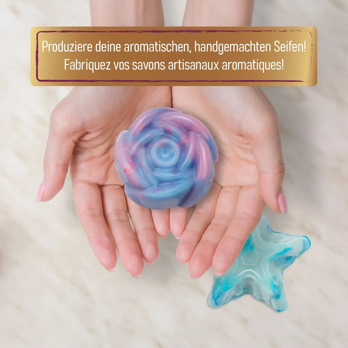 Hände halten eine rosafarbene und blaue Seife in Rosenform, eine Seife in Seesternform liegt daneben