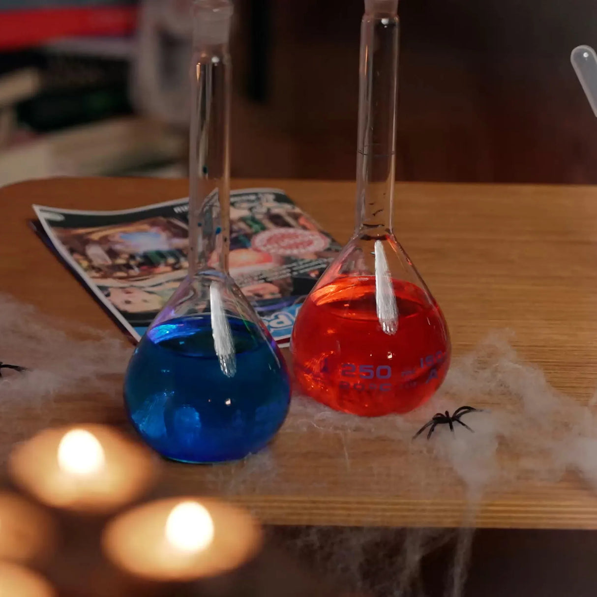 Zwei Erlenmeyerkolben mit blauer und roter Flüssigkeit auf einem Tisch mit Spinnweben und Kerzen