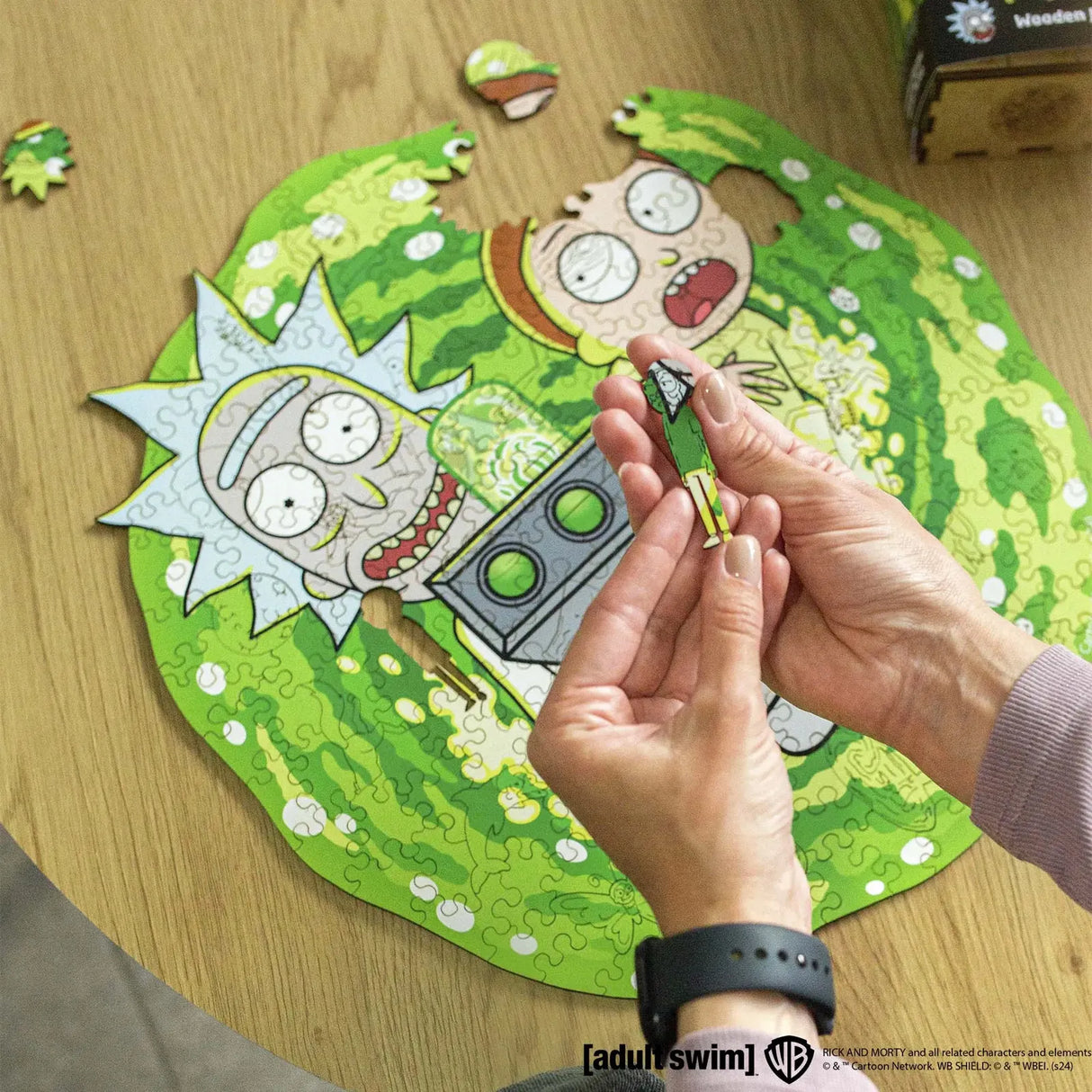 Hände halten ein Rick and Morty Puzzle-Teil über einem teilweise zusammengesetzten Puzzle