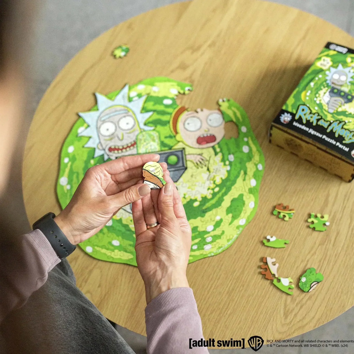 Hände halten ein Puzzleteil mit Rick und Morty auf einem grünen Portal-Puzzle