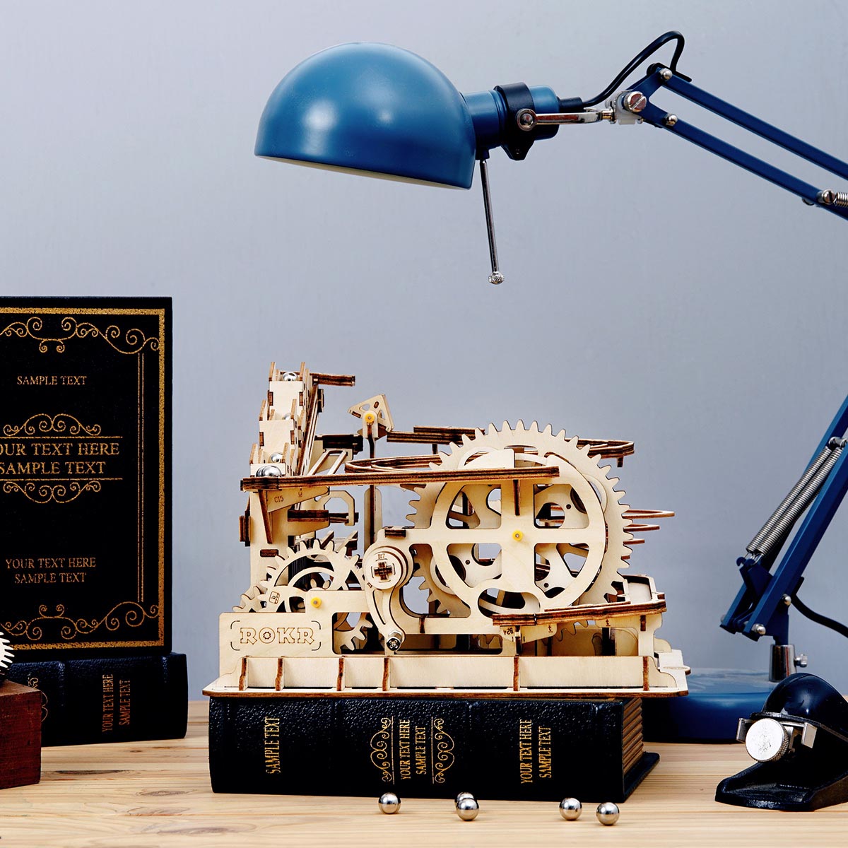Mechanisches Holzmodell einer Kugelbahn auf einem Buch stehend unter einer blauen Schreibtischlampe