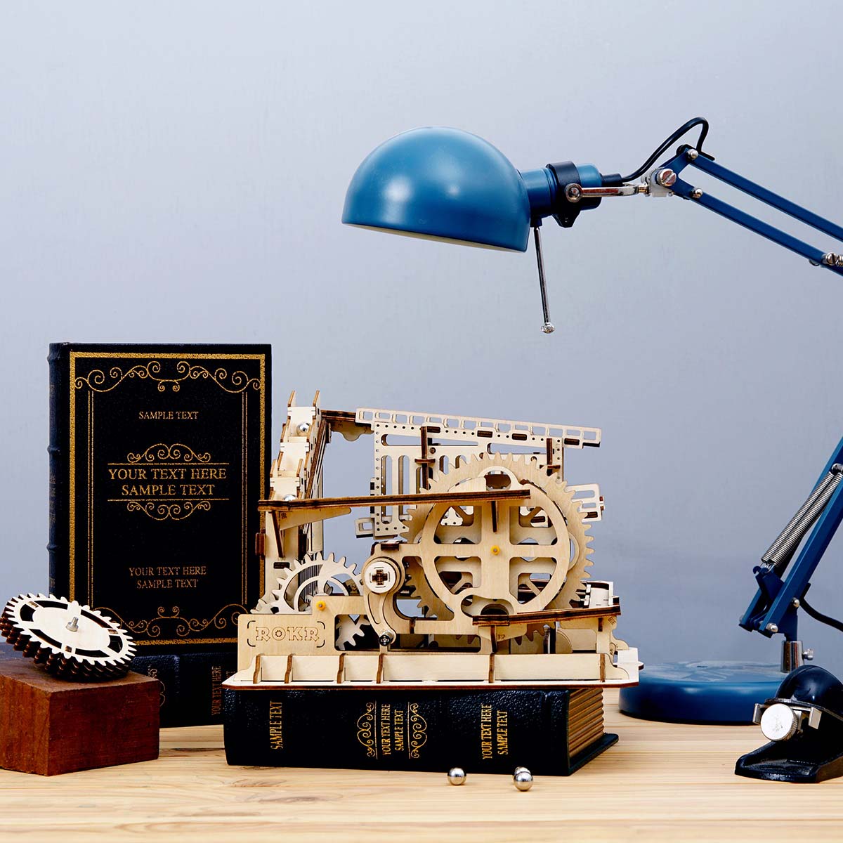 Mechanisches Holzmodell mit Zahnrädern neben einem Buch und einer blauen Schreibtischlampe