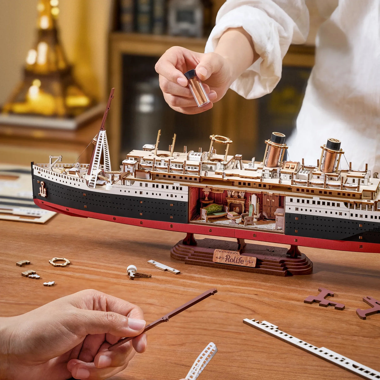 Hände bauen ein detailliertes Holzmodell der Titanic mit sichtbaren Innenräumen und kleinen Teilen auf einem Tisch